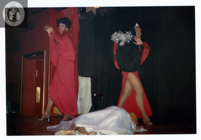 Three people on small stage with one laying on floor at Men's Center Fundraiser, 1982