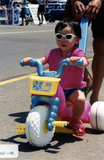 Child in sunglasses on plastic tricycle in Pride parade, 2000