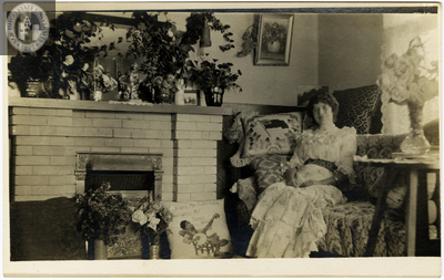 Woman sitting on settee next to fireplace, 1916