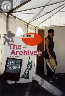 Jules Wertis next to Lesbian and Gay Archives exhibit sign at Pride festival, 1991