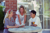 Students read a paper at an outside table, 1996