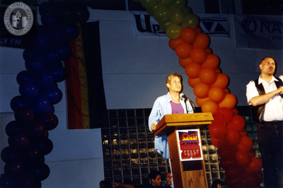 Greg Louganis speaking at lectern on stage at Pride event, 1997