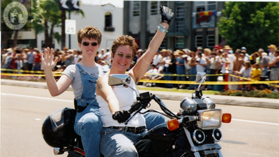 Women wave while riding a motorcycle in Pride parade, 2001