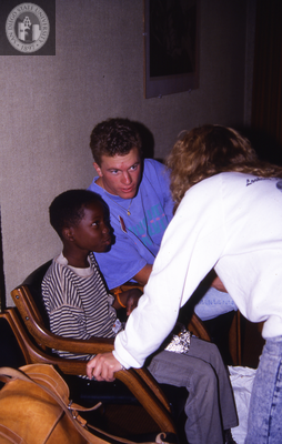 An adult man and child listen to a woman, 1990