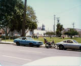 Two cars and motorcycle parked at staging area of Pride parade, 1978
