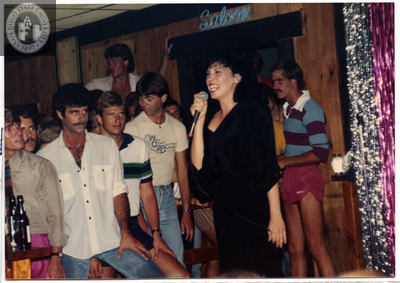 Person with microphone in front of "Saloon" sign, 1982