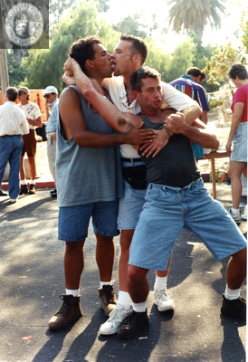 Two men kissing while wrestling third male at Pride parade, 1996