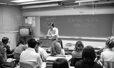 Instructor behind desk in classroom, 1973