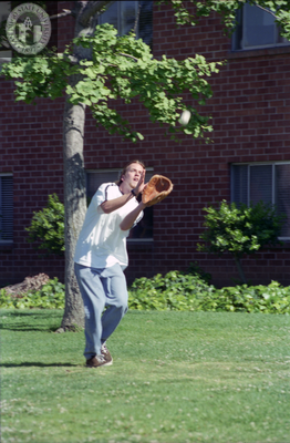 Student plays softball beside brick dormitory, 1996
