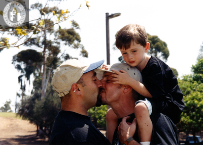 Male couple kissing while carrying child on shoulders, 1996