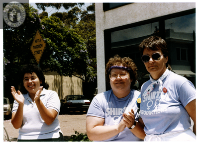 Three women clapping with "Shirtails Productions" shirts at Pride parade, 1988