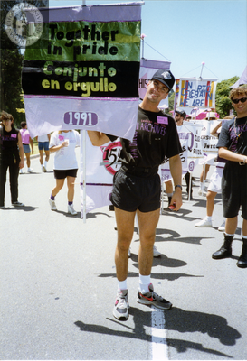Marcher with Lesbian and Gay Archives of San Diego holds flag, 1992
