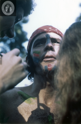 Two people paint someone's face and chest at the San Diego Gay-In, 1970