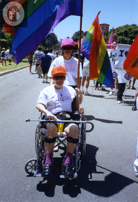 Person in wheelchair with rainbow flag and pusher in Pride parade, 1992