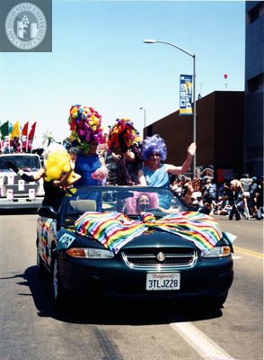 Bewigged individuals in car with rainbow-colored bow at Pride parade, 1997