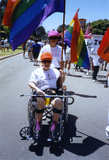 Person in wheelchair with rainbow flag and pusher in Pride parade, 1992