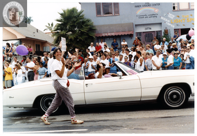 Person claps and walks next to a convertible in Pride parade, 1998