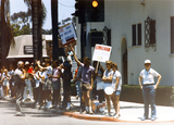 Parade watchers holding pro-LBGTQ signs on sidewalk at Pride parade