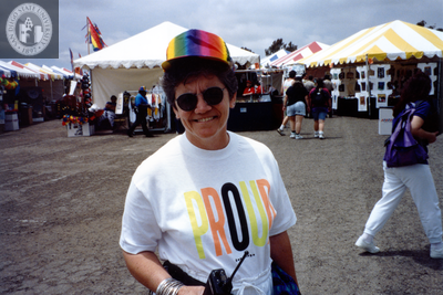Person smiling, standing in front of booths at Pride festival, 1992