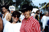 Two people smiling in front of crowd and line of booths at Pride festival, 1992