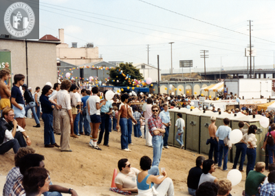 Crowd of people sitting and standing on dirt slope at Pride festival, 1982