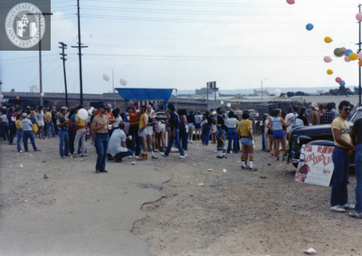 Crowd of people in dirt parking lot area at Pride parade, 1982