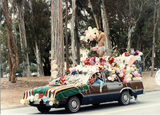 Man atop balloon-and-flower-covered car